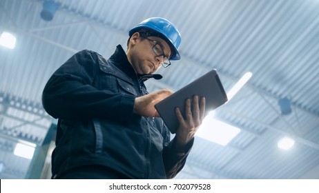 Factory Worker In A Hard Hat Is Using A Tablet Computer.