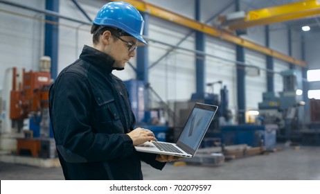 Factory Worker In A Hard Hat Is Using A Laptop Computer With An Engineering Software.