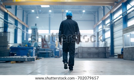 Factory worker in a hard hat is walking through industrial facilities.