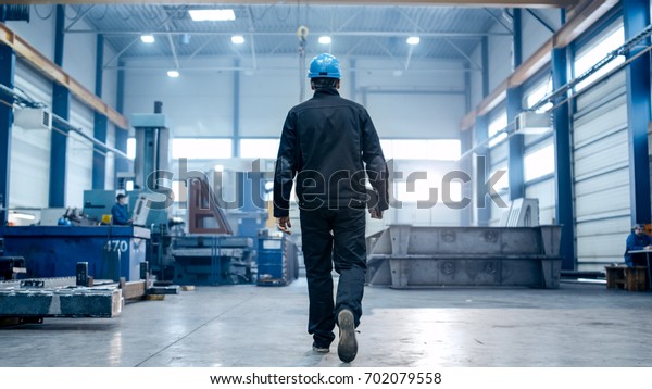 Factory worker in a hard hat is walking\
through industrial\
facilities.