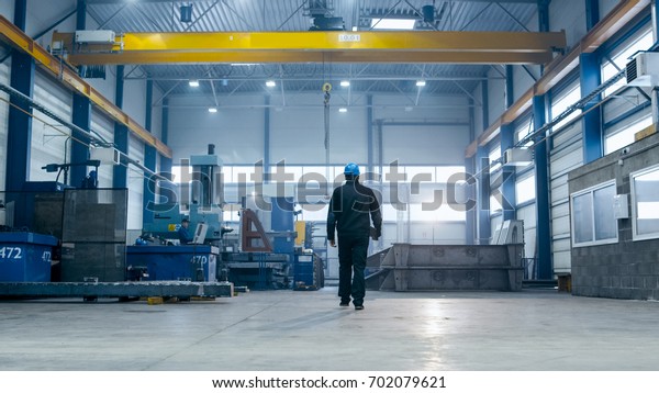 Factory worker in a hard hat is walking\
through industrial\
facilities.