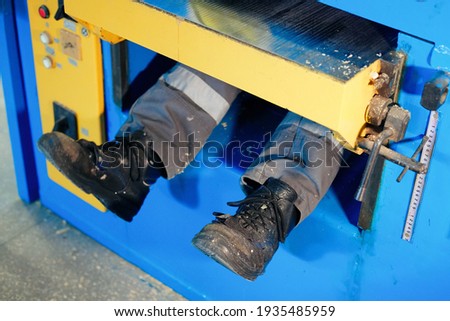 A factory worker was injured in an accident due to non-compliance with safety regulations. The worker is pulled into the lathe, and only the legs stick out. Staged photo. The concept of safety first .