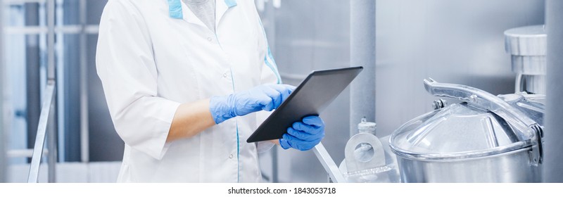 Factory Worker Inspecting Production Line Tanker In Of Dairy Factory With Computer Tablet. Concept Food Industry Banner.