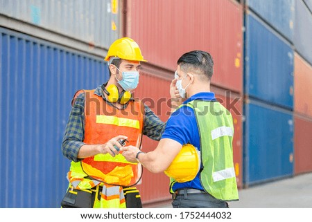 Factory worker man checking fever by digital thermometer for scan and protect from Coronavirus (COVID-19) at cargo containers - Healthcare Concept