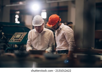 Factory worker man and engineer manager working together a metal sheet industrial worksite , checking machine process on laptop and wearing hard hat for safety