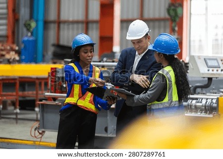 factory worker, manager, and engineer reviewing manufacturing industry safety protocols on tablet while wearing hardhat and vest, showing professional engaged teamwork during discussion.
