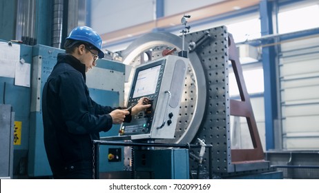 Factory worker is programming a CNC milling machine with a tablet computer.