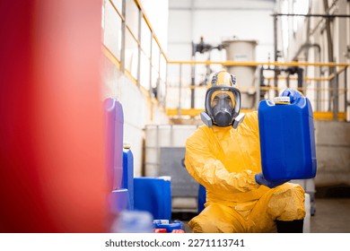 Factory worker in protective equipment and gas mask holding plastic can with chemicals and approving quality.