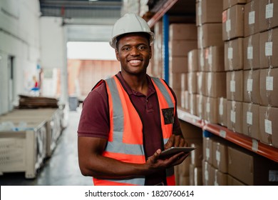 Factory worker smiling holding digital tablet organising parcels in warehouse