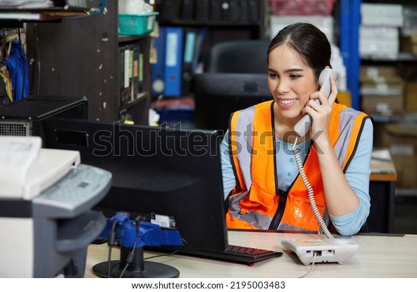 factory worker speaking\
on the telephone and looking at computer monitor in the office or\
warehouse storage