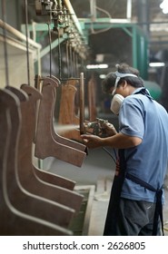 Factory Worker Spray Painting Furniture Parts At An Assembly Line