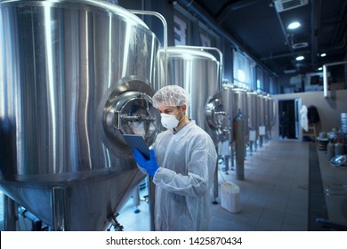 Factory worker technologist in protective uniform with hairnet and mask controlling food production on tablet computer. - Powered by Shutterstock