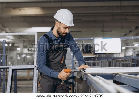 Factory worker using electric screwdriver assembling aluminum window frames in production line at workshop