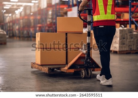 Factory worker using hand pallet truck to move carton box in warehouse. Close up scene in logistics and distribution center showing manual labor.