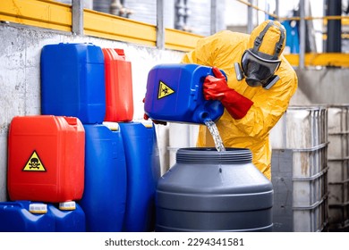 Factory worker wearing yellow protection suit and gas mask working in chemicals production plant handling acids.