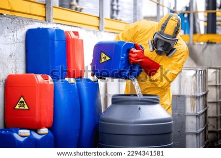 Factory worker wearing yellow protection suit and gas mask working in chemicals production plant handling acids.