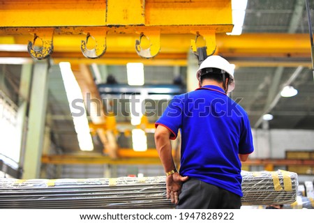 factory worker working with hooks from a crane lifting of round steel bars and place on a truck at warehouse.