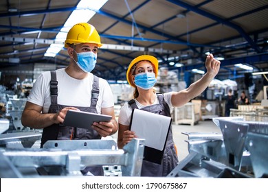 Factory workers with face masks protected against corona virus doing quality control of production in factory. People working during COVID-19 pandemic.