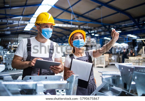 Factory workers with face masks\
protected against corona virus doing quality control of production\
in factory. People working during COVID-19\
pandemic.