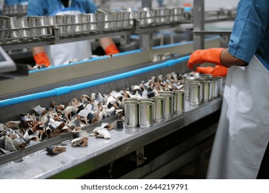 Factory workers in gloves sort and package fish for canning on a production line. The atmosphere is busy as they ensure quality and efficiency in the processing of seafood.