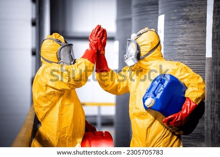 Factory workers in protection suit and gas mask greeting with hands inside chemicals factory.