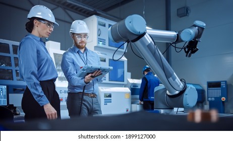 Factory Workshop: Professional Female Engineer, Male Machinery Operator Use Industrial Digital Tablet Computer to Work and Program Robot Arm for Production Line. High-Tech Facility with CNC Machines - Shutterstock ID 1899127000