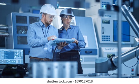 Factory Workshop: Professional Female Engineer, Male Machinery Operator Use Industrial Digital Tablet Computer to Work and Program Robot Arm for Production Line. High-Tech Facility with CNC Machines - Shutterstock ID 1899127018