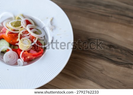 Factual, sharp angle view of a fresh vegetable salad with tomatoes, cucumber, pepper, and onion rings served in a textured white plate on a wooden table, reference file