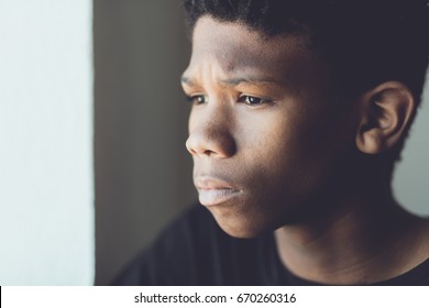 Faded retro portrait of a worried young African boy staring off to the side with a sad expression and frown in a close up side view