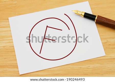 A failing grade, A white card with text of  F and a fountain pen on a wooden desk