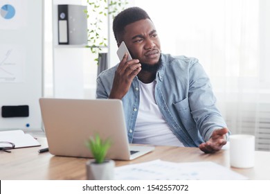 Failure And Crisis Concept. Upset African American Employee Getting Bad News On Phone While Sitting At His Workplace In Office, Copy Space