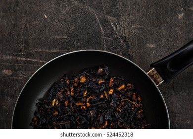 The Failure On Kitchen: Burnt Charred Vegetables. Frying Pan With Refried Black Onion And Overcooked Orange Carrots. Cooking Fail Concept Background With Copy Space.