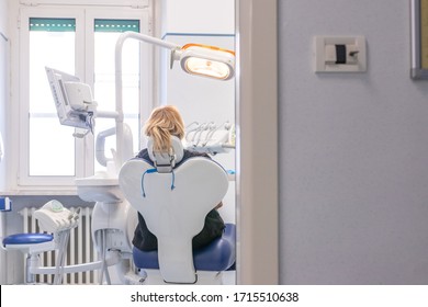 Fair Haired Woman Waiting In Hospital Chair For Annual Dental Examination And General Check Up. Back Shot, White Natural Lighting, High Tech Medical Interiors. Health Insurance System In Europe, Italy