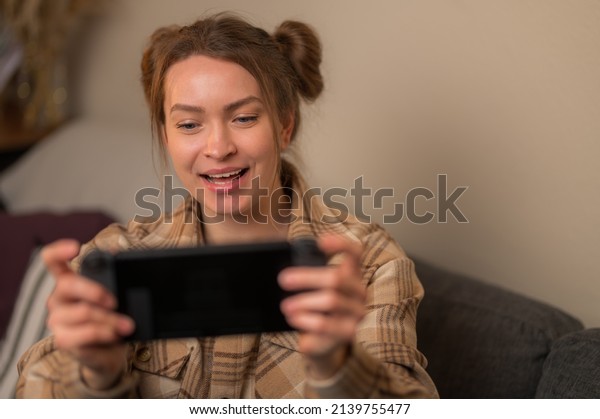 A\
fair-haired girl gamer has fun playing mobile games on a portable\
game console. Online technology, fun with friends, small business,\
freelancing, virtual reality, esports, game\
strategy.