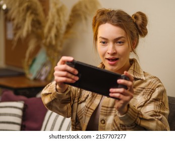 A fair-haired pretty girl plays an interesting adventure game with friends online on a portable game console at home, in the living room. Communication, competition, prizes, win, surprises.