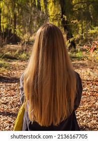 A fair-haired woman with long flowing hair stands on a sunny day in an autumn park. Back view. The concept of naturalness