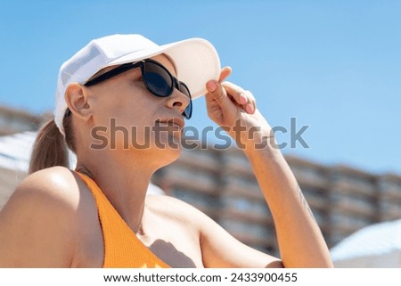 A fair-skinned girl, wearing a white cap and sunglasses, sits on the beach in a swimsuit against a backdrop of blue sky, epitomizing summer serenity. Stock photo © 