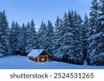 Fairy Christmas landscape with glowing wooden cabin in snowy forest. Cozy house in winter mountains