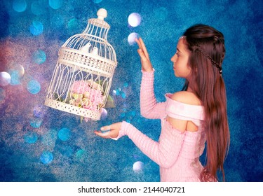 Fairy girl creates a miracle. A beautiful cage with two doves and a bouquet of flowers flies. Photo shoot in the studio on a blue background with bright sparkles and confetti.