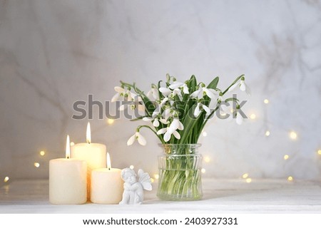 fairy girl figurine, snowdrops flowers and candles on table, light abstract background. spring season. Romantic composition with flowers. relaxation, dreams, love, hope concept