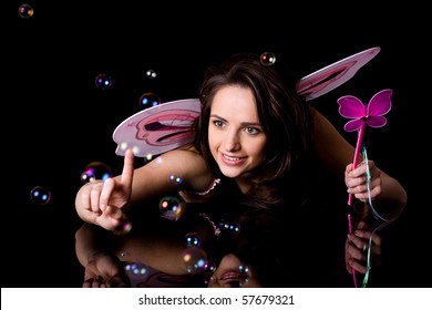 fairy with pink wings and magic wand trying to catch bubbles, studio shoot isolated on black