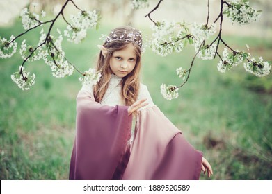 Fairy Tale Girl. Portrait Of Mystic Elf Child. Cosplay Character. Portrait Of Elf In Blooming Cherry Garden. Girl With Long Ears Touches Flowers Of White Flowers
