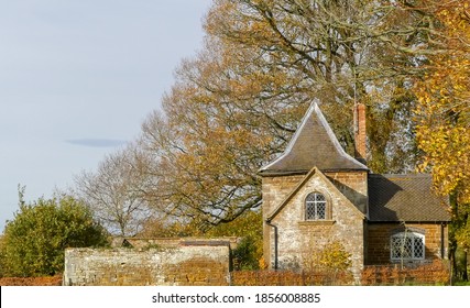 Fairy Tale  Old Gothic Style Cottage Built In Local Stone With Unusual Roof. Under Trees With Leaves In Autumn Colour. Blue Sky With Single Cloud. Landscape Image With Space For Text. England.