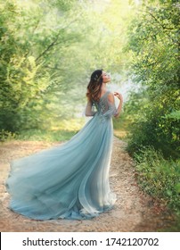 Fairy Tale Princess In Light Summer Blue, Turquoise Dress Standing In Park. Happy Woman Walks Towards Wind. Fashion Model Posing. Fantasy Image Girl Goddess. Flying Long Hem Of Dress. Nymph Of Forest