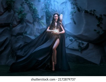 Fairy Woman Elf Queen In Black Fantasy Sexy Long Dress Fly In Wind Cape Flutter Waving Flowing Around Witch. Princess Goth Girl Sharp Ears Golden Crown. Old Style Cave. Spell Light In Hand Dark Magic 