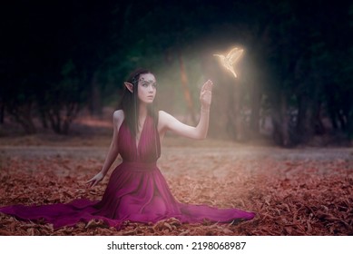 Fairytale Elven Princess With A Magic Bird In A Dark Forest. Night In The Forest.Summer Nature Forest Green Tree.Autumn Leaves. Long Hair, Pointed Elf Ears, Green Eyes, Jeweled Tiara.