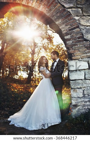 Fairytale romantic valentyne newlywed couple hugging and posing under old castle bridge at sunset in autumn
