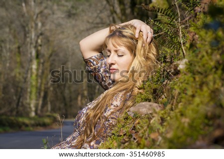 Fairytale scene of a young woman laying in the forest on hill with green moss in sunny autumn forest 