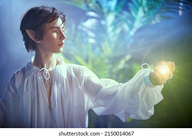 Fairytale young elf looks at the magic light in his hand while standing in the forest. Fairy tale, magic. Fantasy.