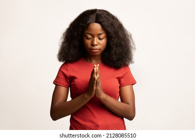Faith Concept. Portrait Of Calm African American Female Praying With Clasped Hands And Closed Eyes, Religious Young Black Woman Standing Isolated Over White Studio Background, Copy Space